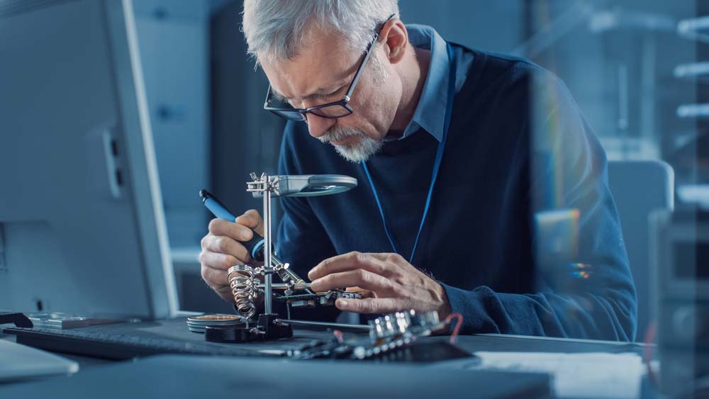 An electronics engineer looking through a magnifying glass to inspect a PCB