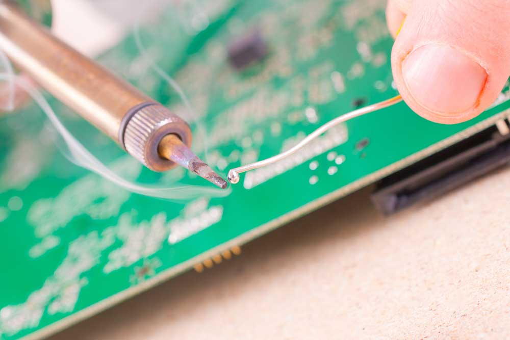 An electrician soldering a wire onto a double-sided PCB