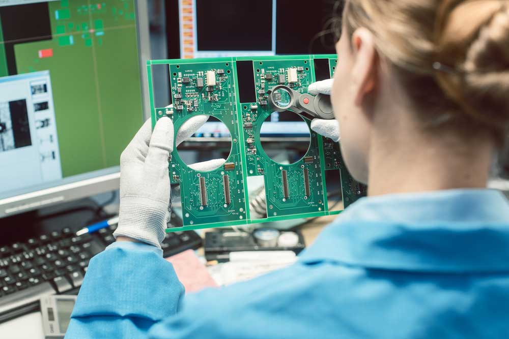 An operator visually inspects a PCB assembly.