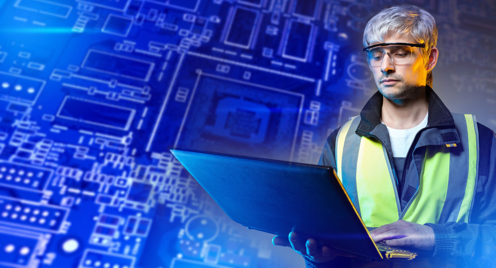 Electronics engineer designing a concept on a laptop with an image of a PCB behind him