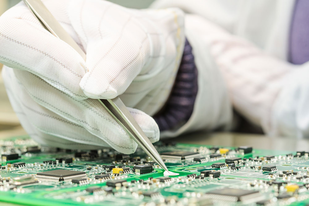 Hand holding a pair of tweezers above a PCB