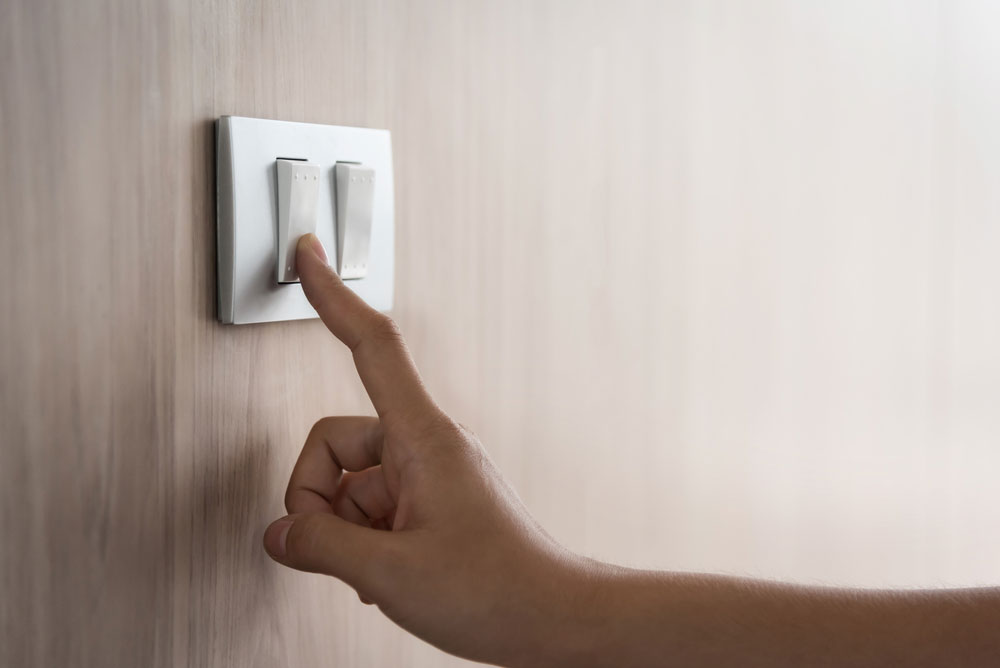 Turning on or off on light switch with wood wall at home.