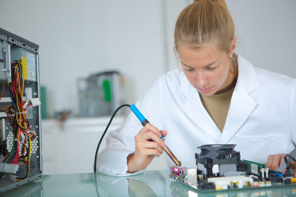 A girl working on a circuit board with a soldering iron