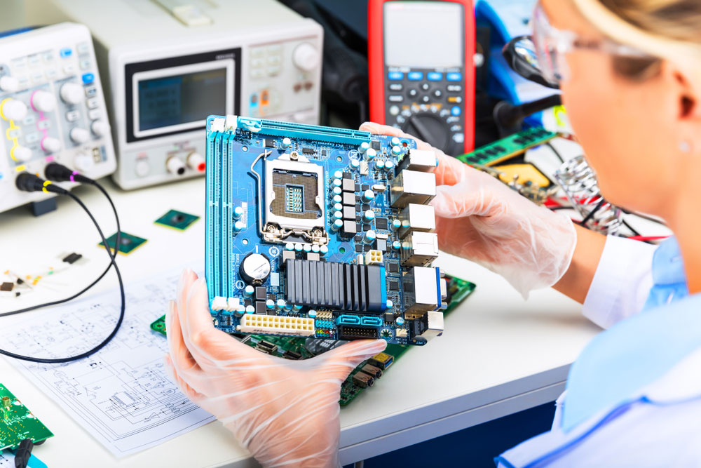 An electronics engineer is examining a computer motherboard. Note the TDR device in the background.