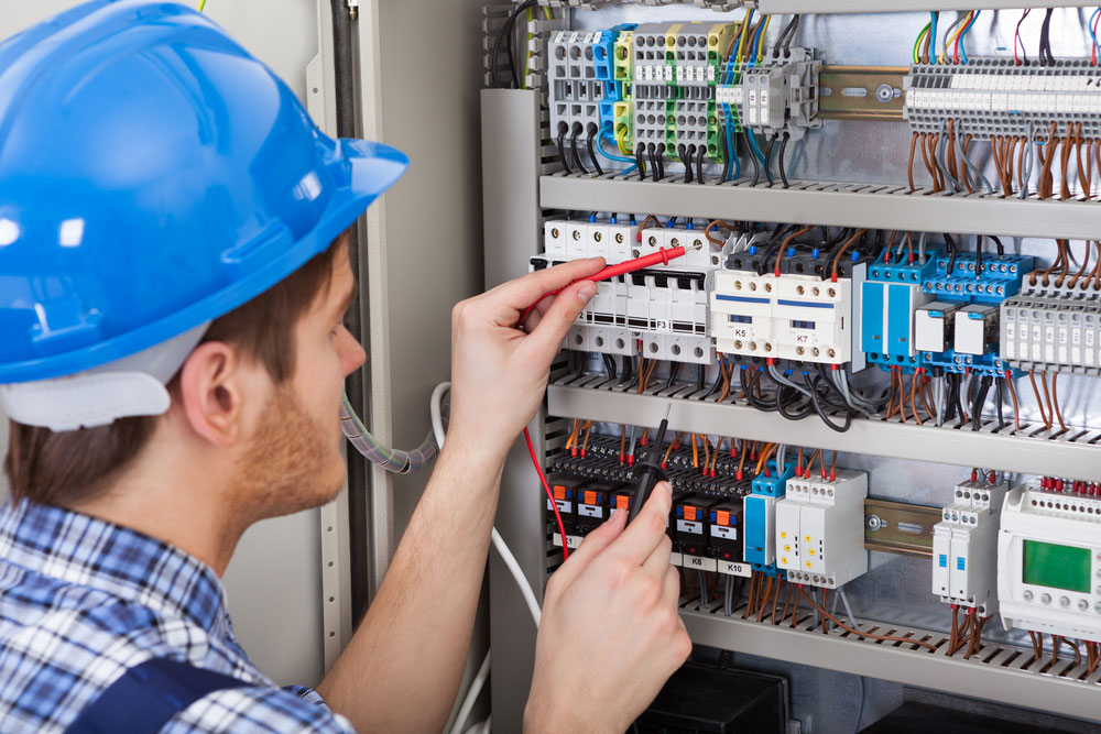 A technician examining a fuse box using a digital multimeter