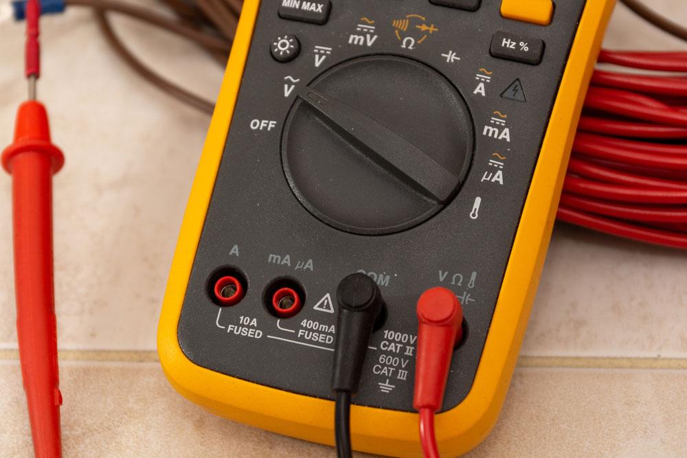 A close-up of a multimeter showing the dial, selectable modes, probes, and four slots