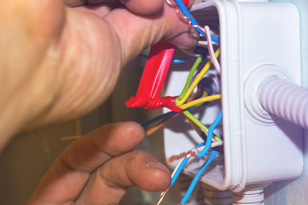 An electrician insulating wire ends using electrical tape in a junction box.
