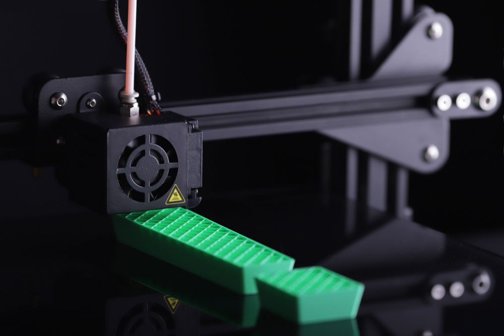 A 3D printer printing an exclamation mark using green plastic