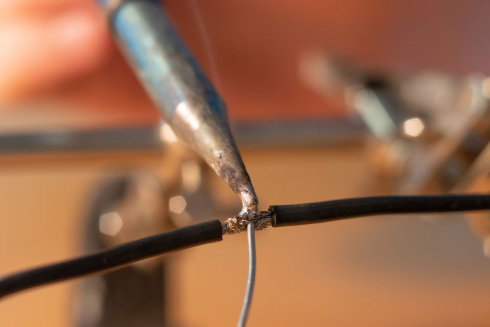 A soldering iron melting solder to join two wires