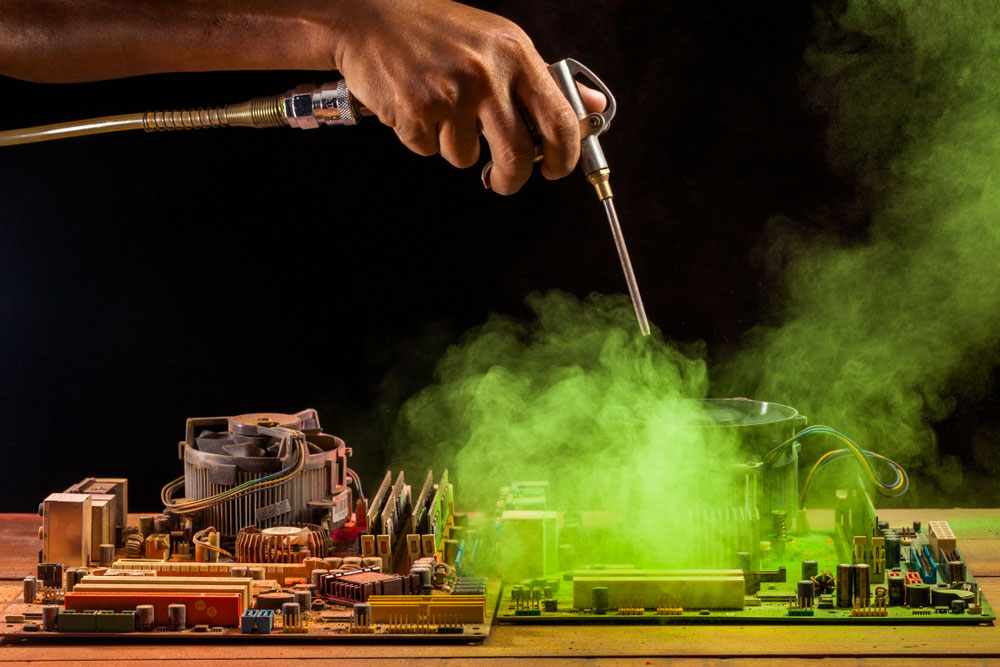 A person cleaning a computer motherboard using an air compressor