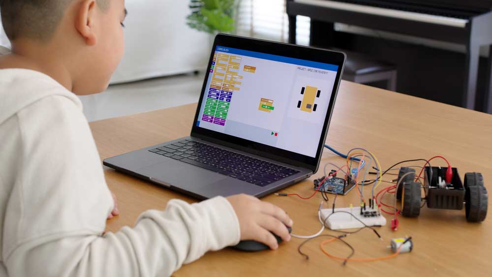 A young kid coding an assembled robot car using block programming (note the Arduino board in the background)